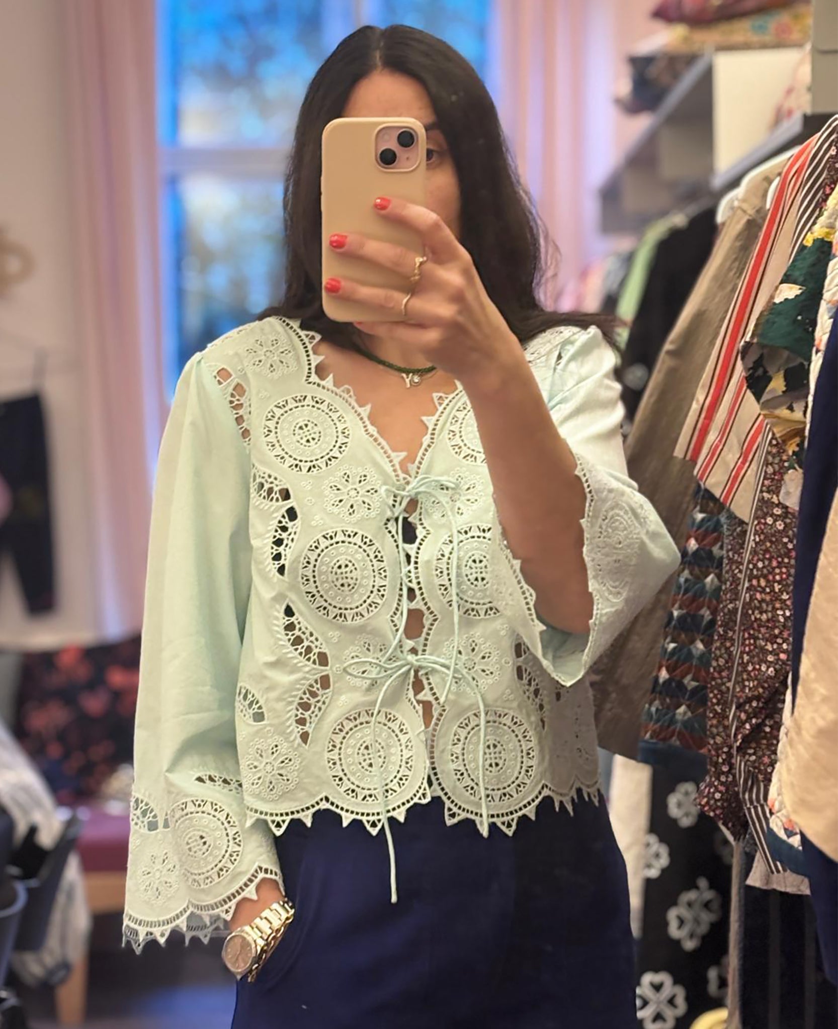 Woman taking a selfie wearing a light blue top with cutwork embroidery and long sleeves with two front ties and navy pants - ANNIE.G