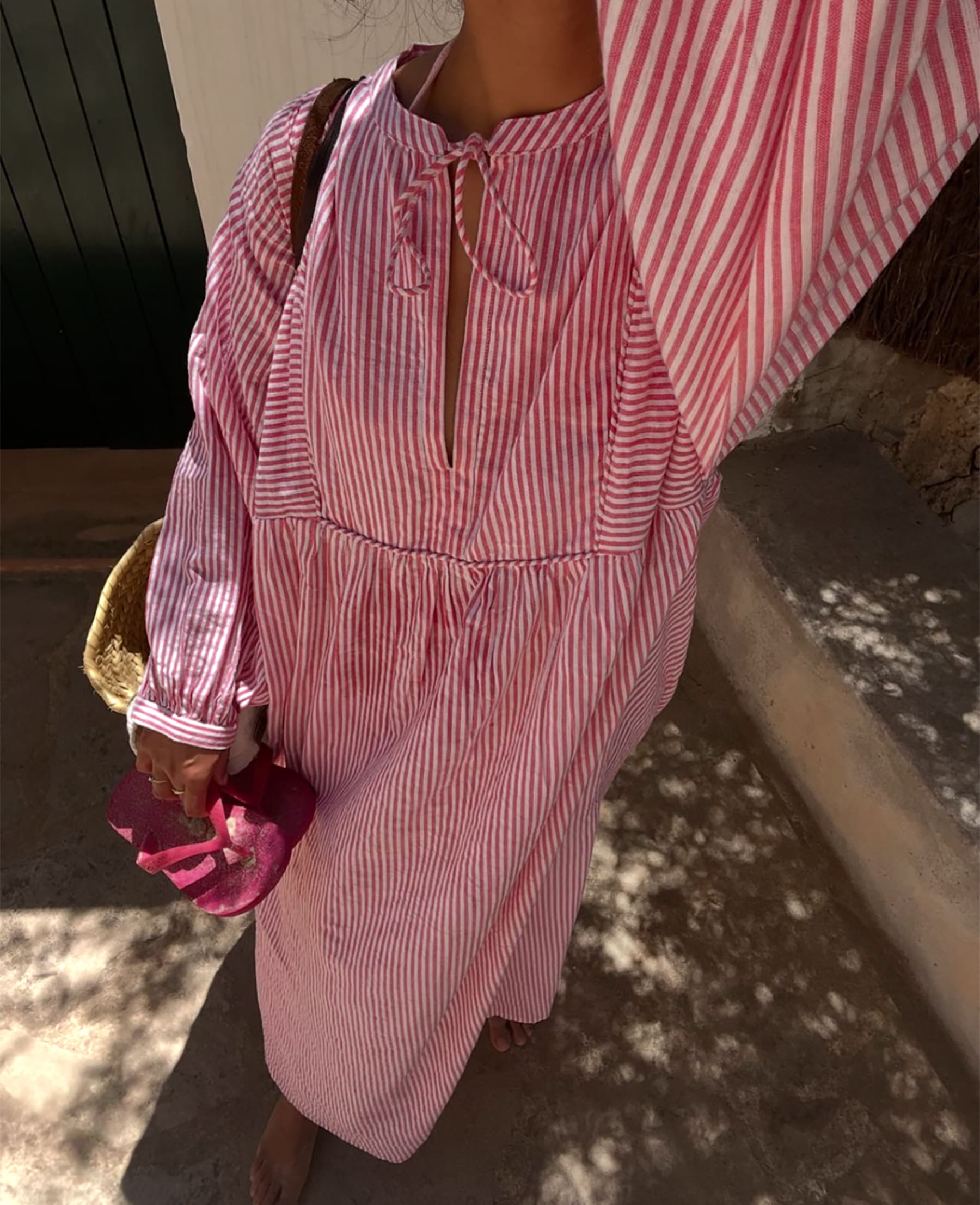 Person wearing a red and white striped dress holding a pink flip flops.