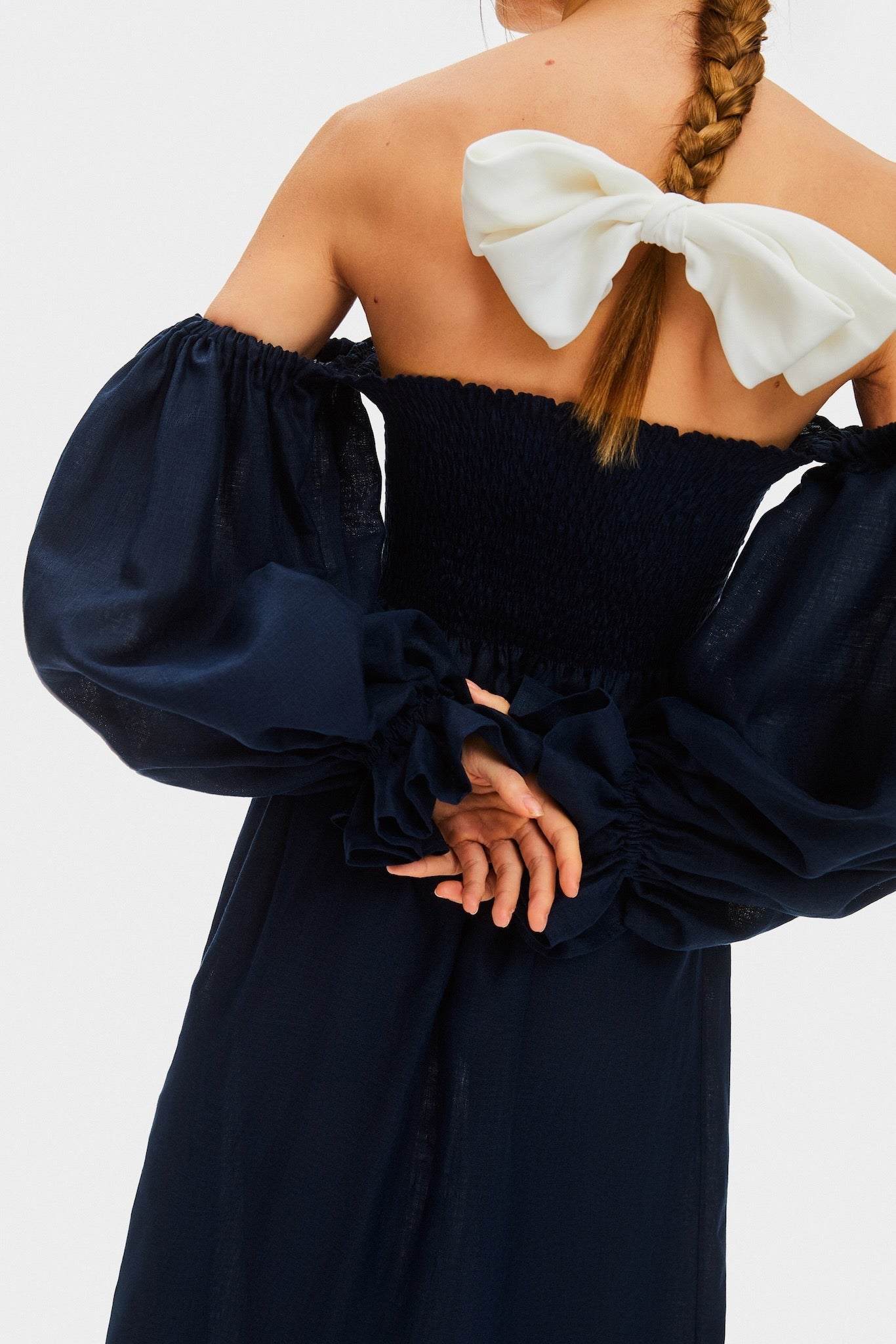 Back of a woman wearing a navy linen dress with smocked bodice and long sleeves.