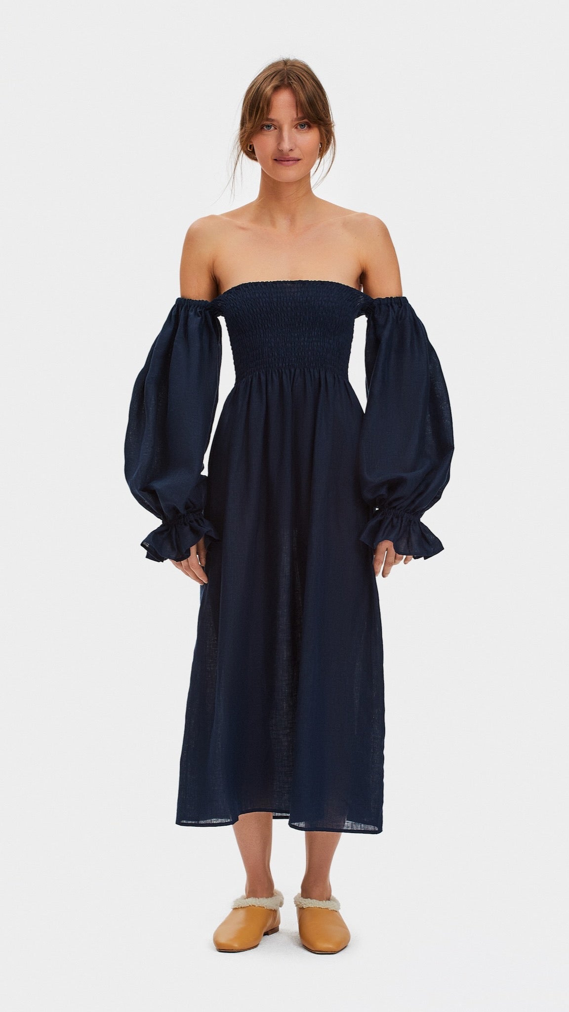 Woman wearing a navy linen midi dress with long off the shoulder sleeves and a smocked bodice.