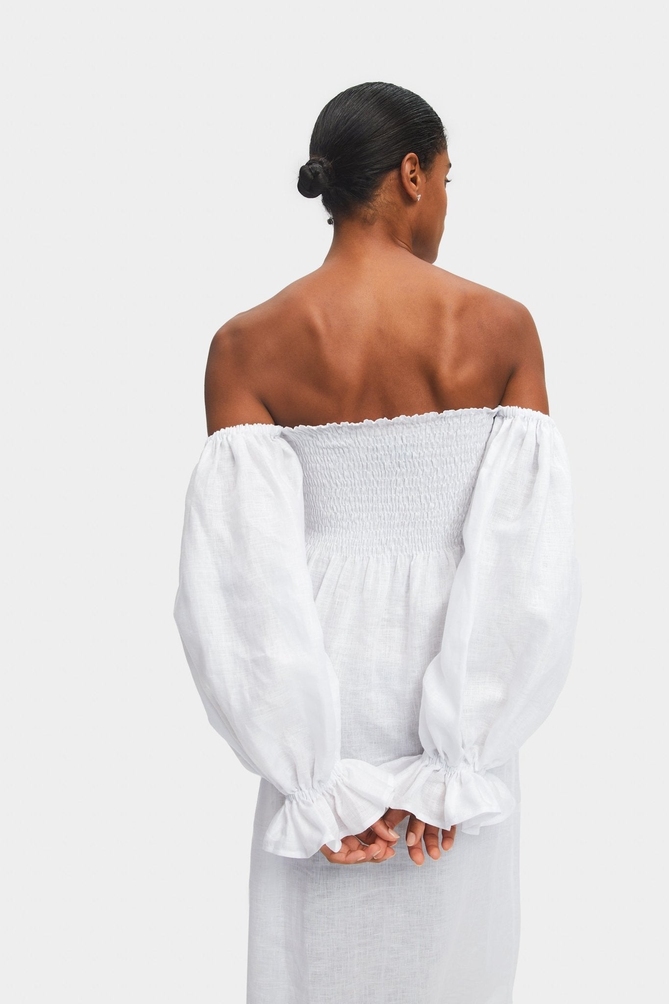 Back of a woman wearing a white off the shoulder dress with smocked bodice and long sleeves with elastic cuff.