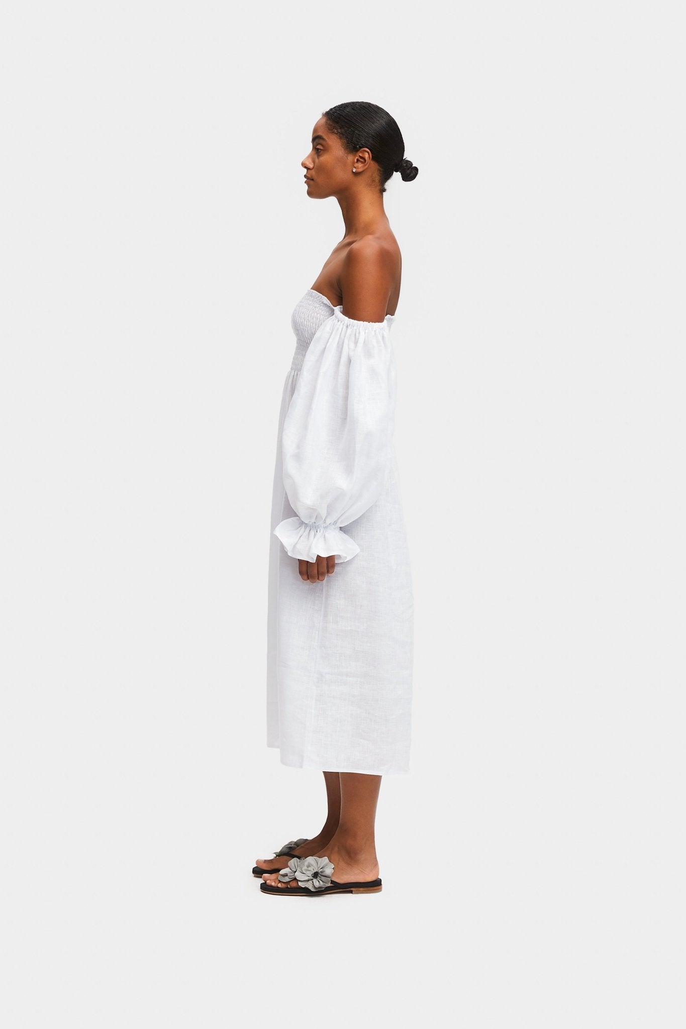 Woman standing on the side wearing a white dress off the shoulder with a long sleeves.