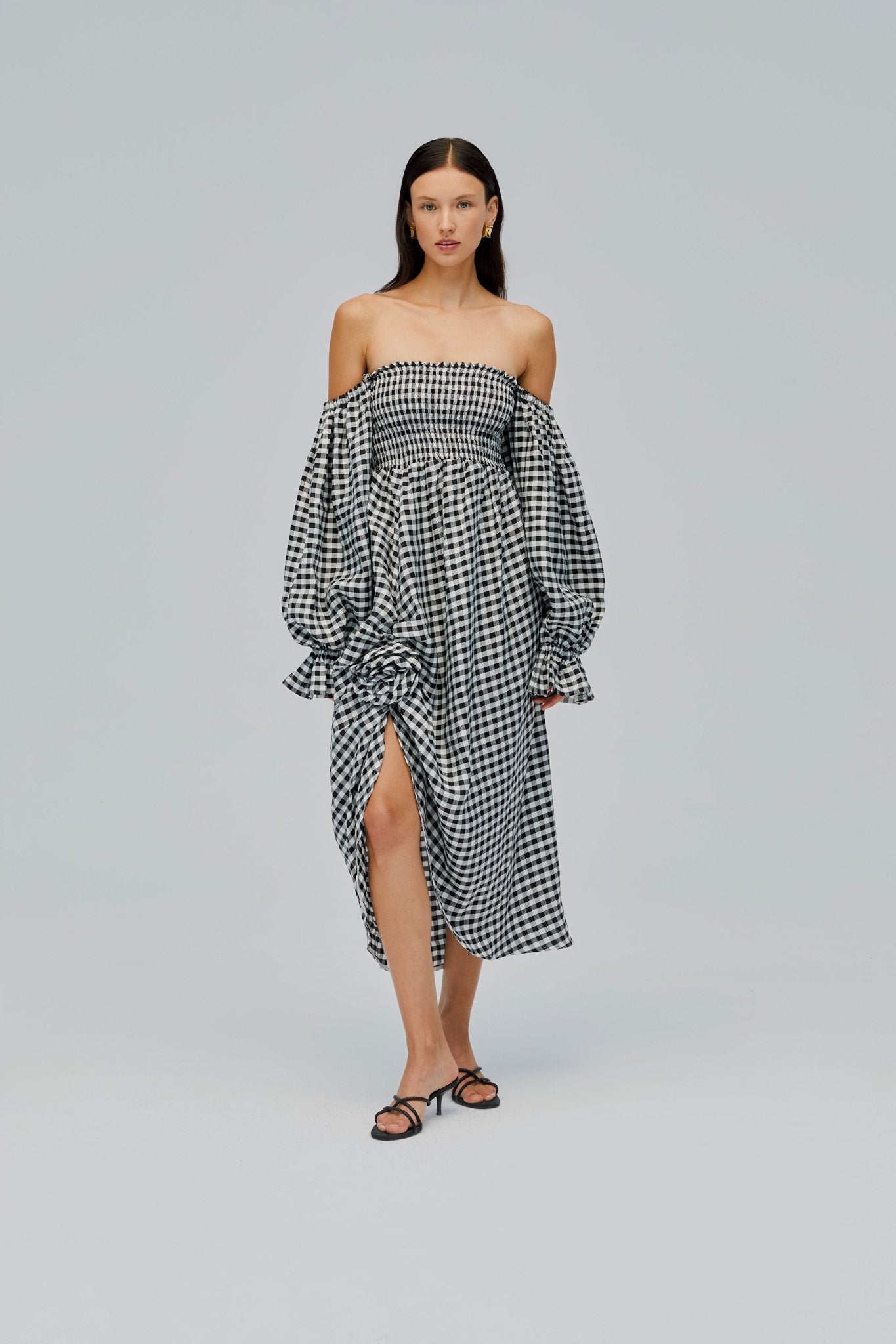 woman wearing a linen, black gingham, long puffed sleeve, off the shoulder dress with a fabric rose at a front split and shirred bust.