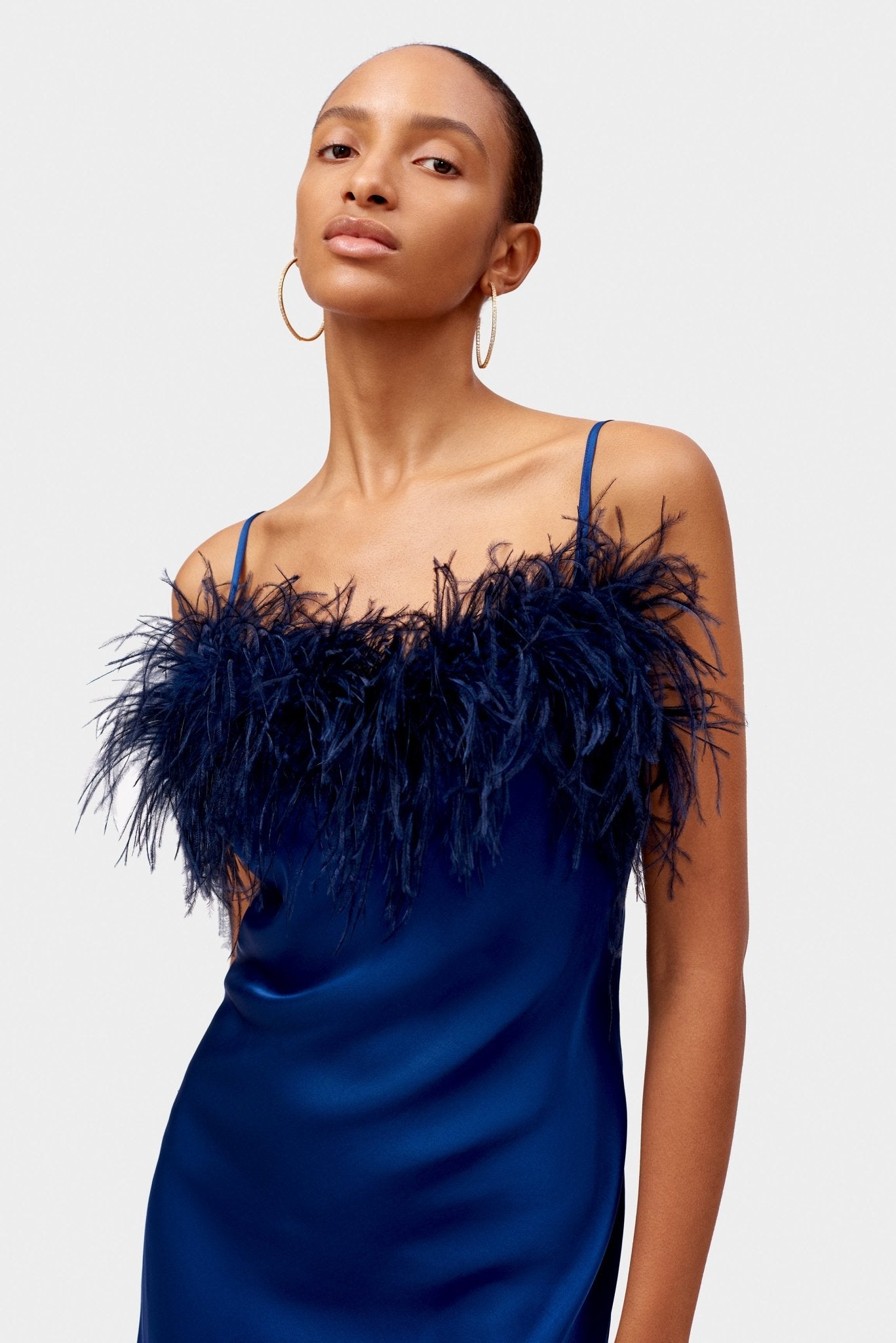 Close up of woman wearing a navy satin mini dress with feathers at neckline and spaghetti straps.