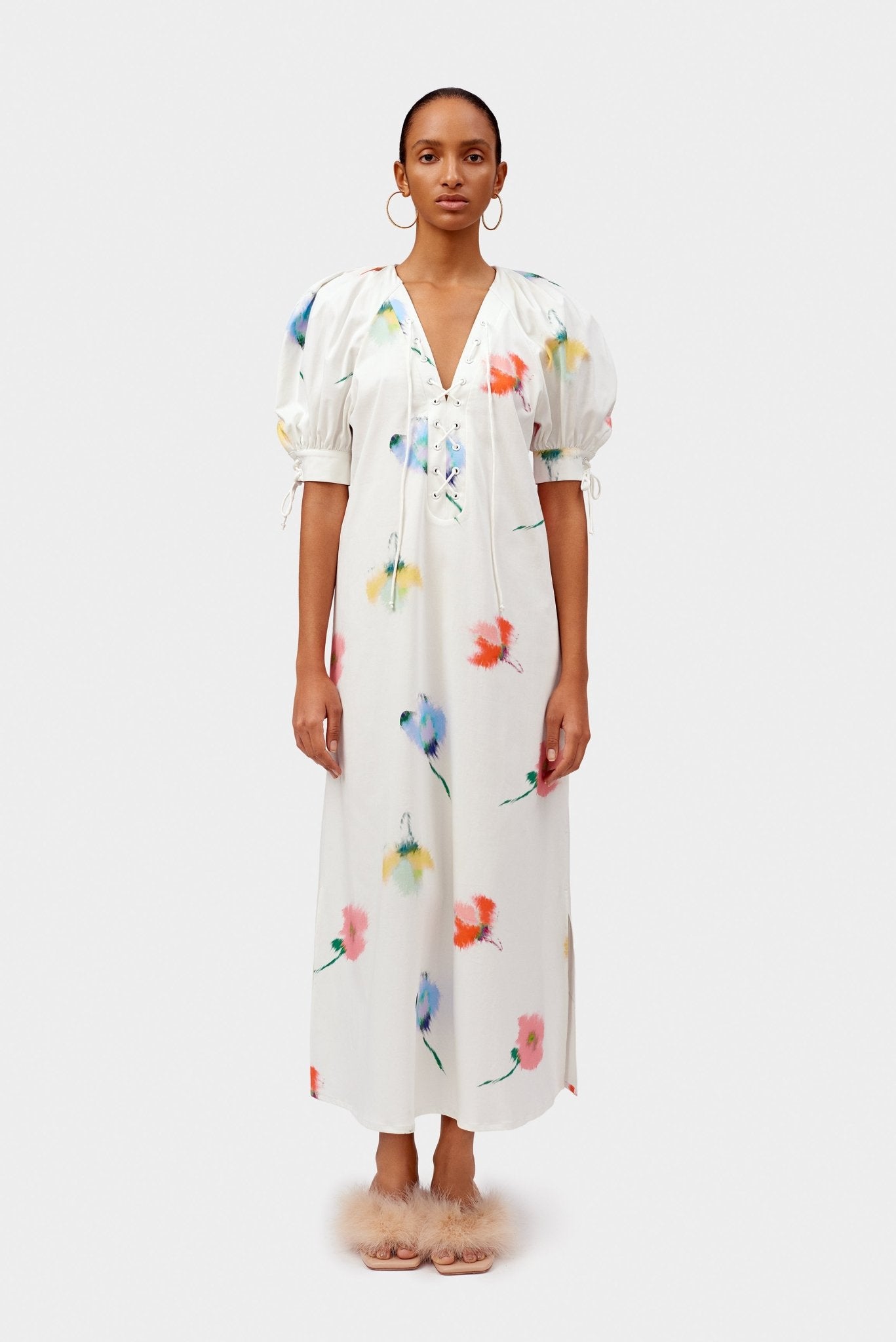 Women wearing a white cotton dress with watercolour flowers print with puff sleeves and v-neck with lacing details.