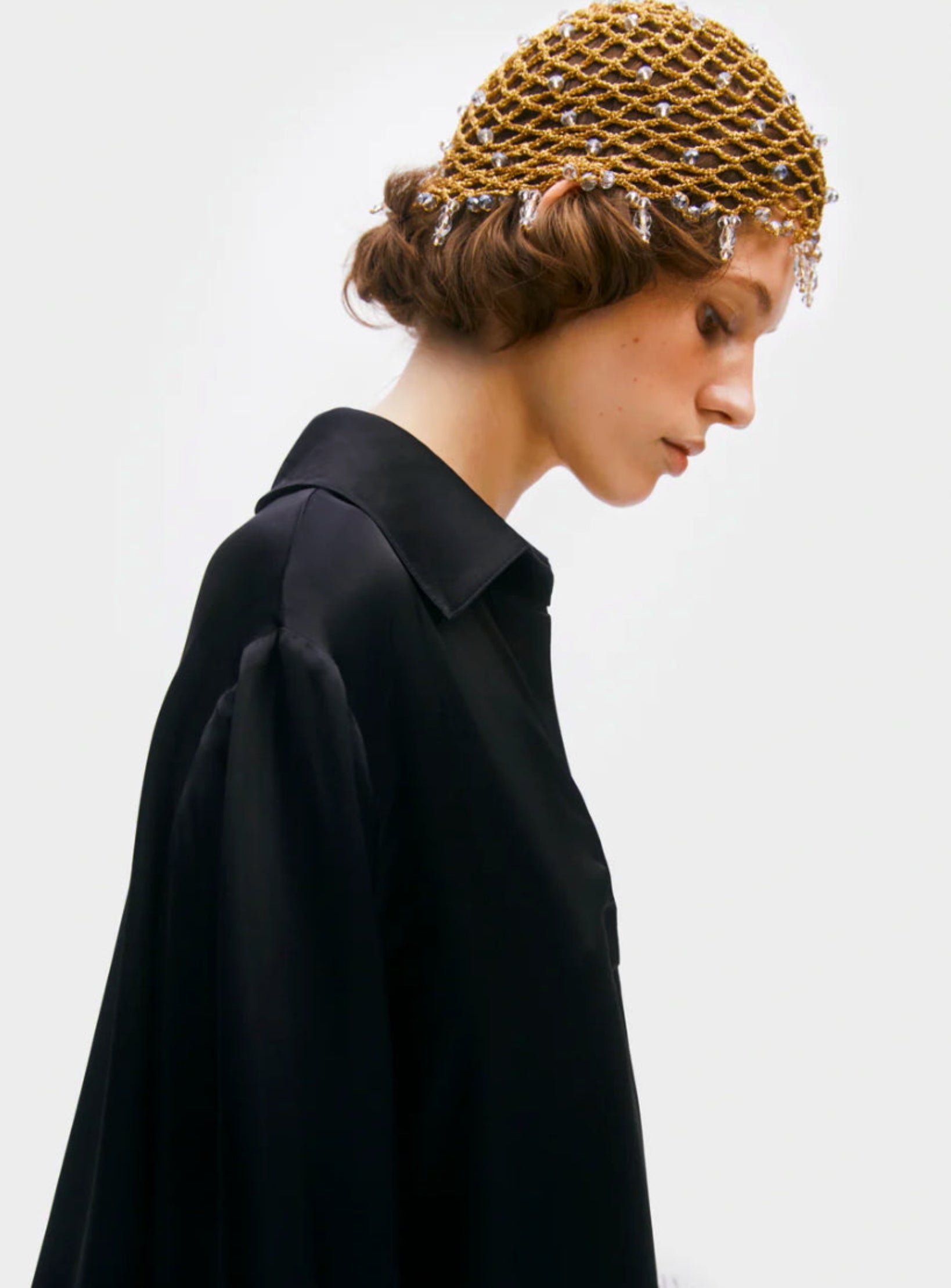 Woman in black loungewear wearing a gold crocheted hat with cystals on head.