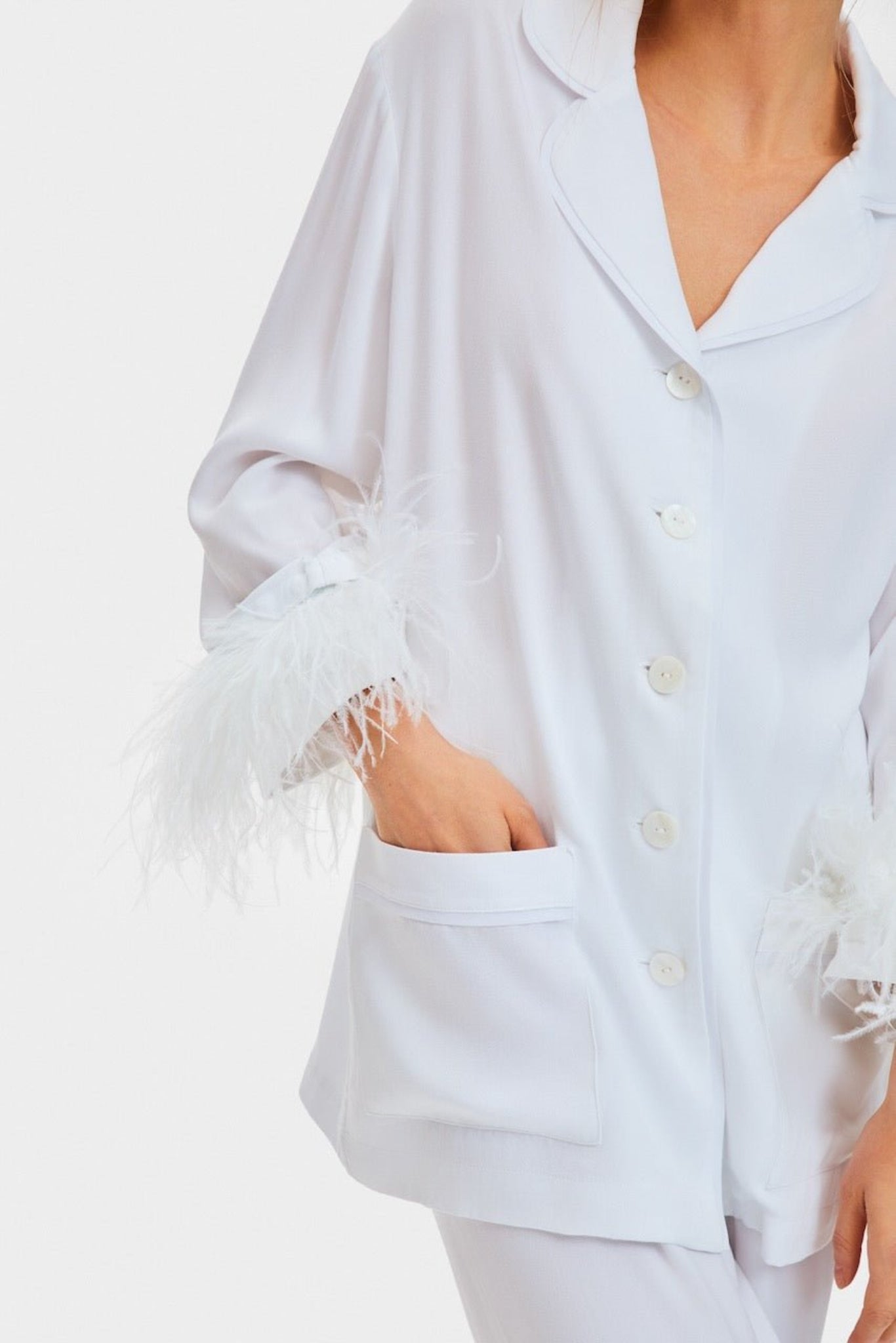 Close up of woman wearing white party pyjama button up shirt and pants with hand in pocket.