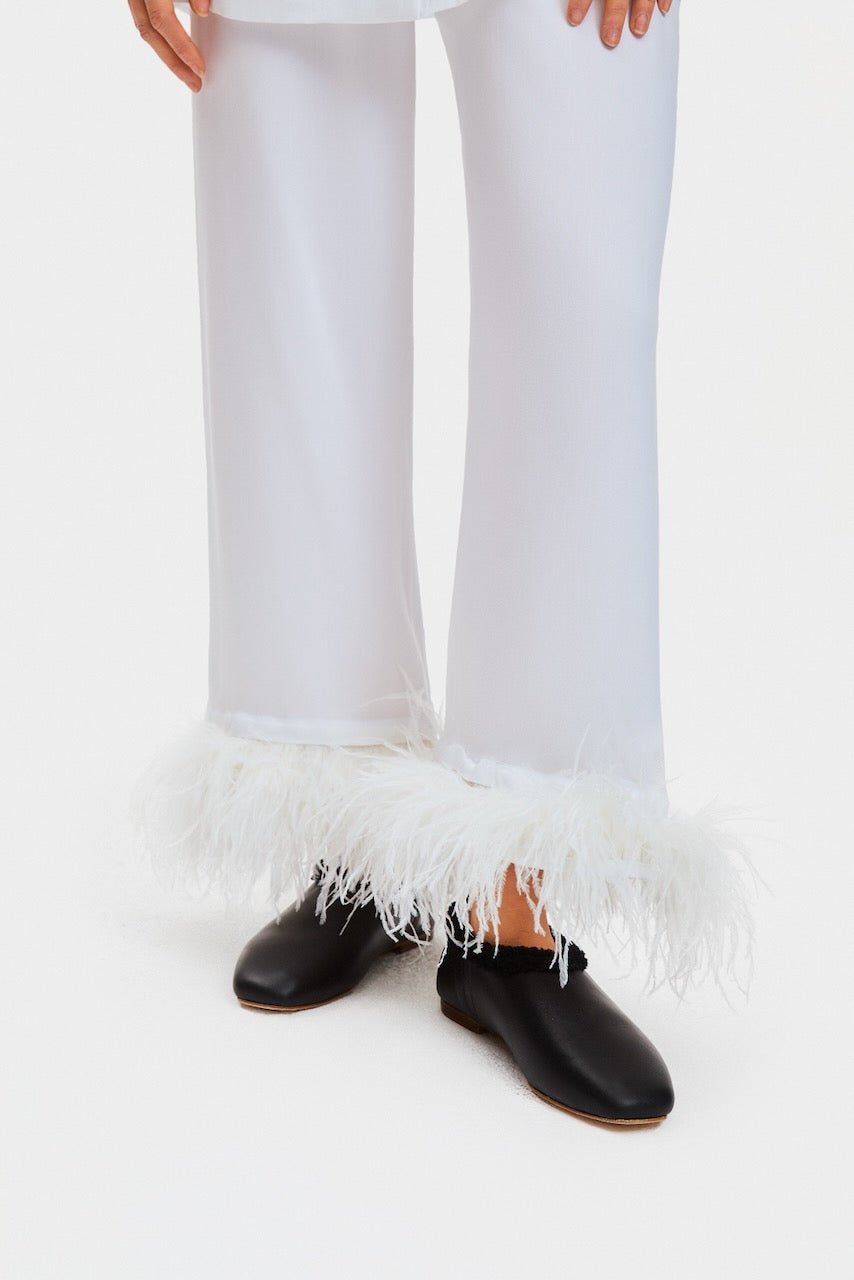 Person wearing white pyjamas pants with Double Feathers and black flat shoes.
