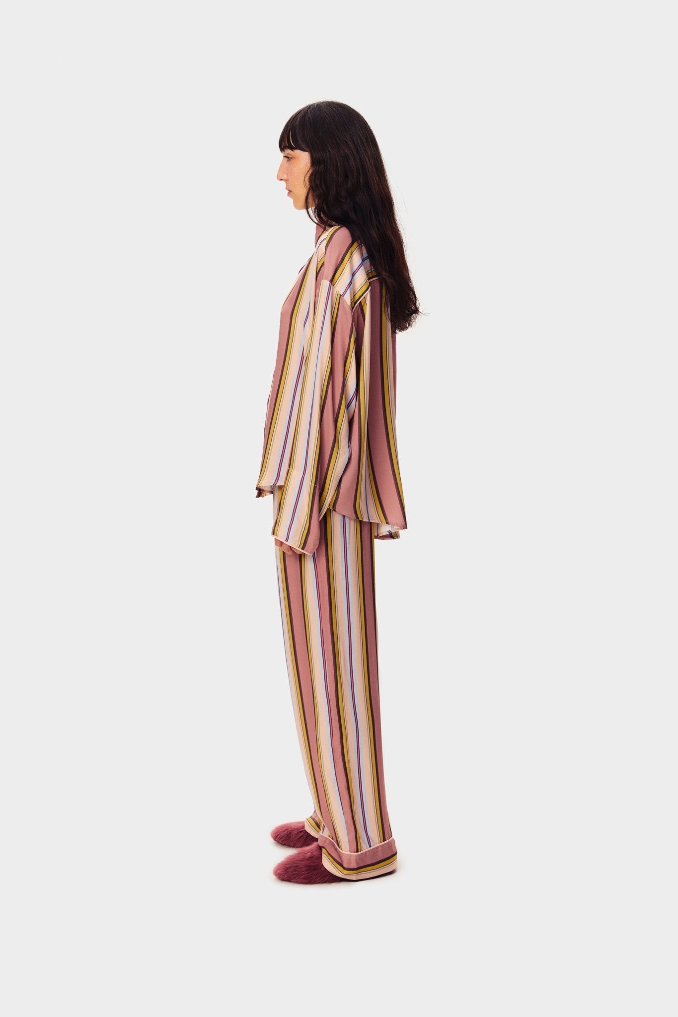 Woman standing on the side wearing pink striped shirt and long pants with slippers.
