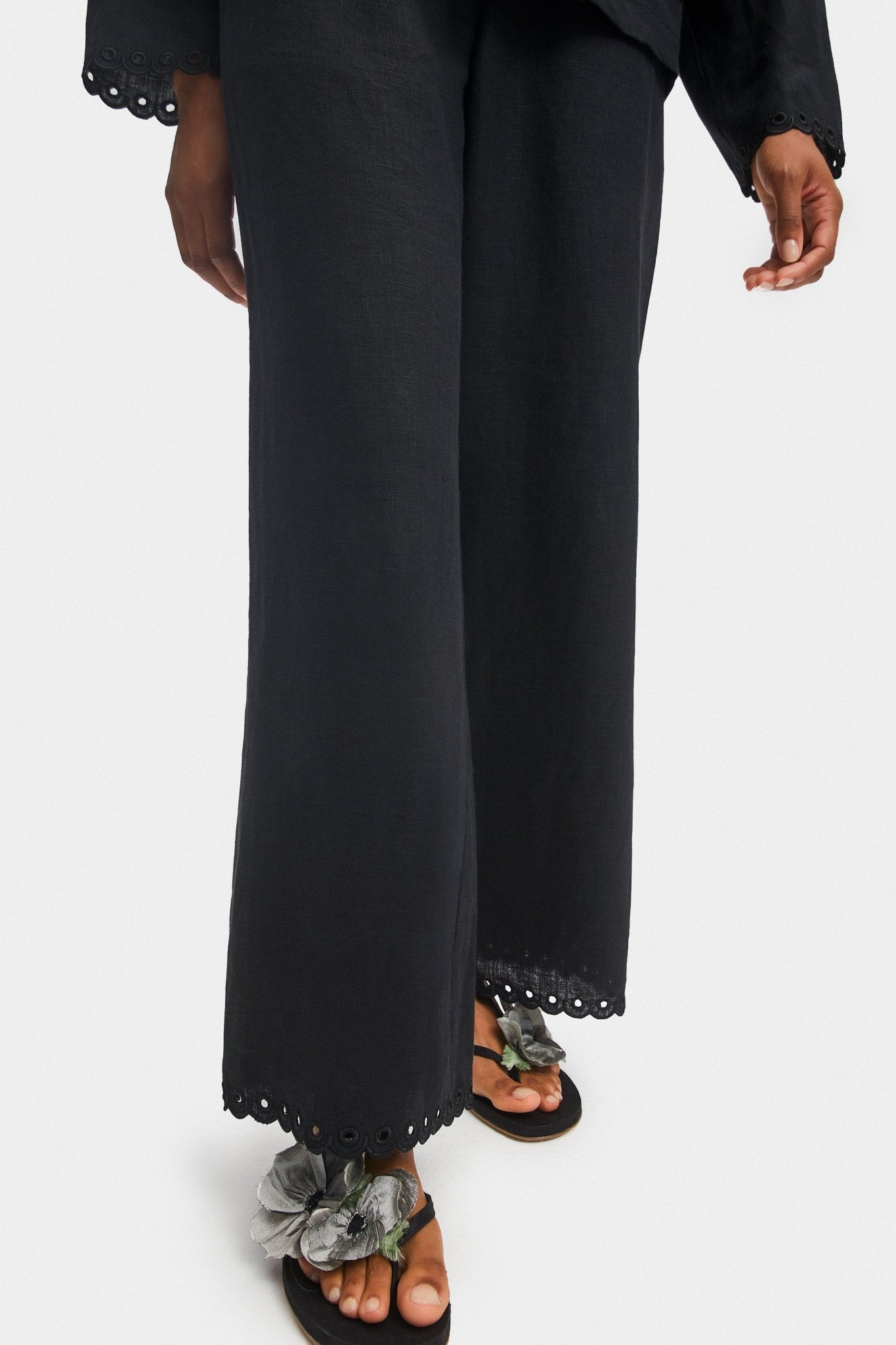 Person wearing black shirt and pants with scalloped embroidered hem and black shoes.