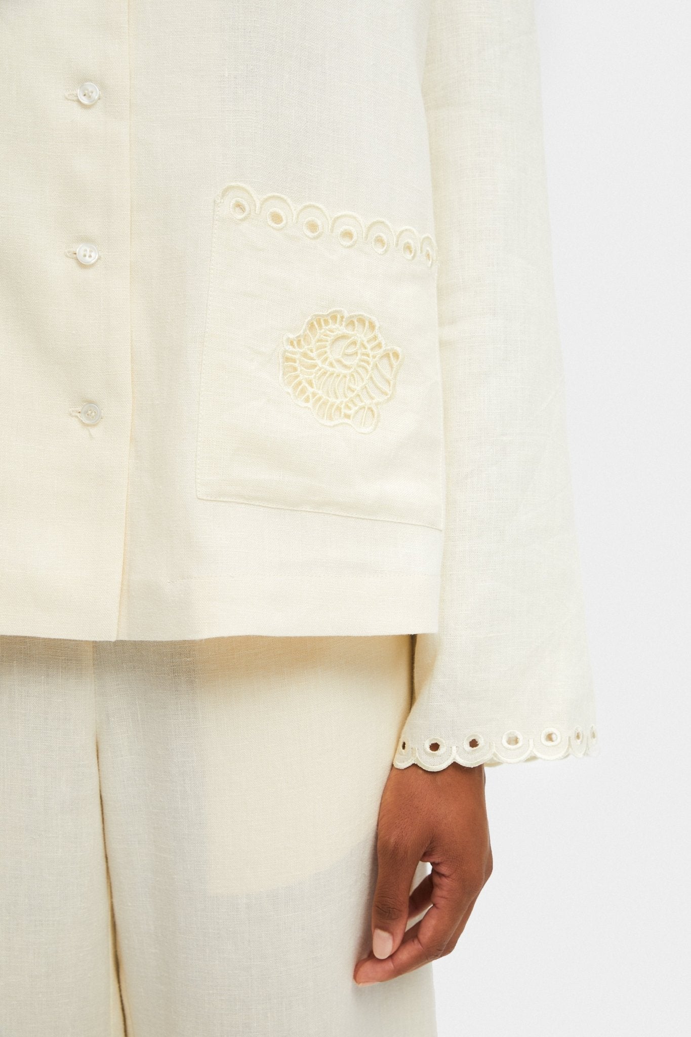 Close up of cream shirt front buttons and embroidered scallop edge on pocket and sleeve.